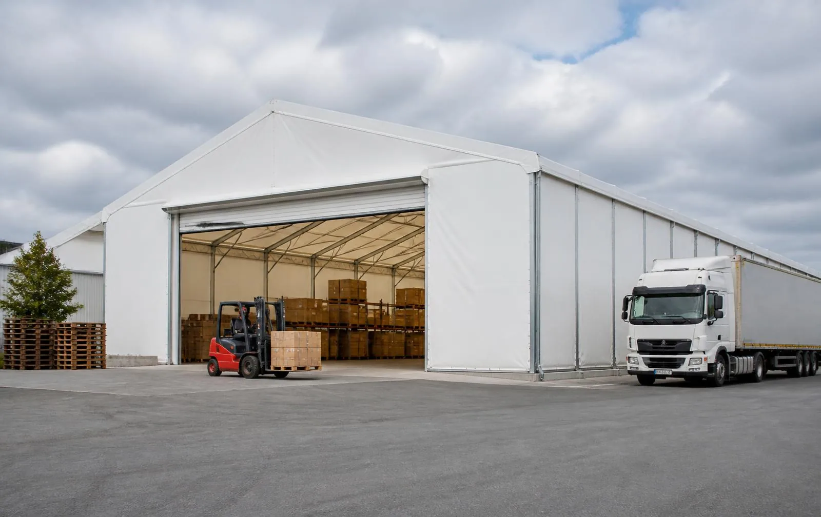 Hangar industriel en PVC blanc avec structure en acier galvanisé sur un parc logistique, portail ouvert avec chariot élévateur et camion en manœuvre